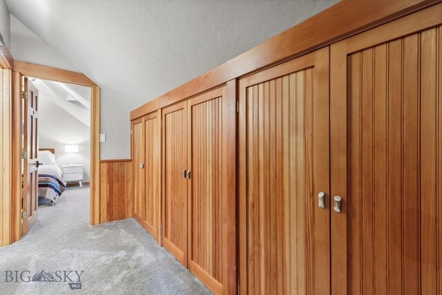 corridor with wood walls, light colored carpet, and lofted ceiling