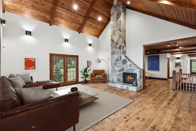 living room with light hardwood / wood-style floors, high vaulted ceiling, wooden ceiling, and a stone fireplace