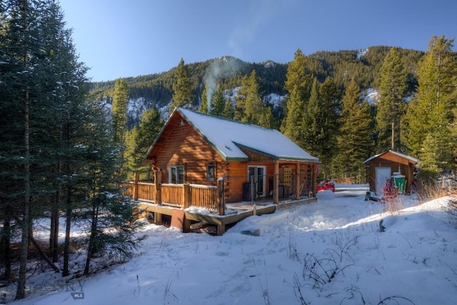 snow covered back of property with a forest view, an outdoor structure, and a deck