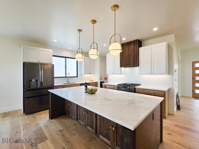 kitchen featuring a kitchen island, refrigerator with ice dispenser, high end black range, and white cabinets