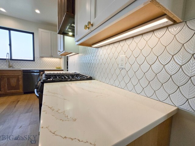 kitchen with light stone countertops, dishwasher, light hardwood / wood-style flooring, sink, and white cabinets