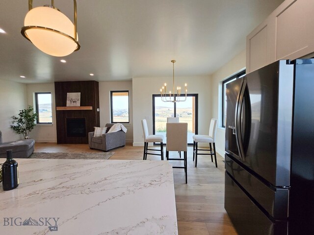 interior space featuring plenty of natural light, pendant lighting, a fireplace, and black refrigerator with ice dispenser