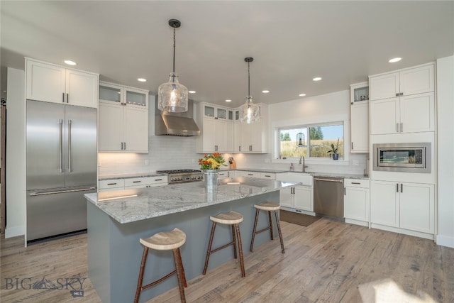 kitchen featuring light hardwood / wood-style floors, white cabinetry, stainless steel appliances, a center island, and wall chimney range hood