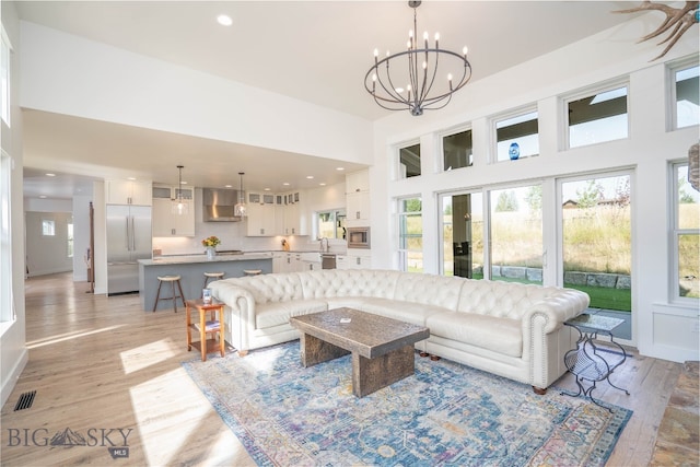 living room with a towering ceiling, an inviting chandelier, light wood-type flooring, and plenty of natural light