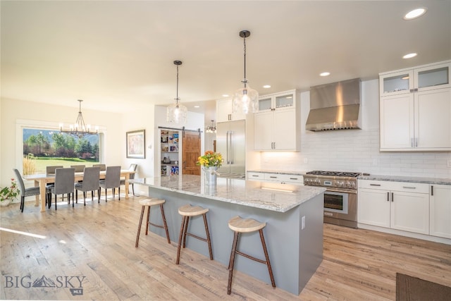 kitchen featuring high end appliances, a kitchen island, light hardwood / wood-style flooring, wall chimney exhaust hood, and white cabinetry