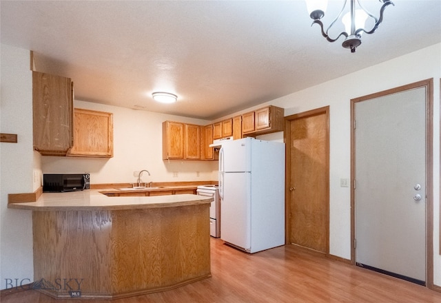 kitchen featuring kitchen peninsula, white appliances, sink, an inviting chandelier, and light hardwood / wood-style floors