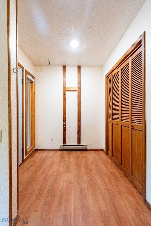 unfurnished bedroom featuring a textured ceiling, light hardwood / wood-style flooring, a closet, and a baseboard heating unit