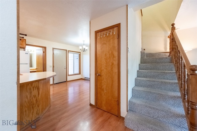 stairs with wood-type flooring, baseboard heating, and a chandelier