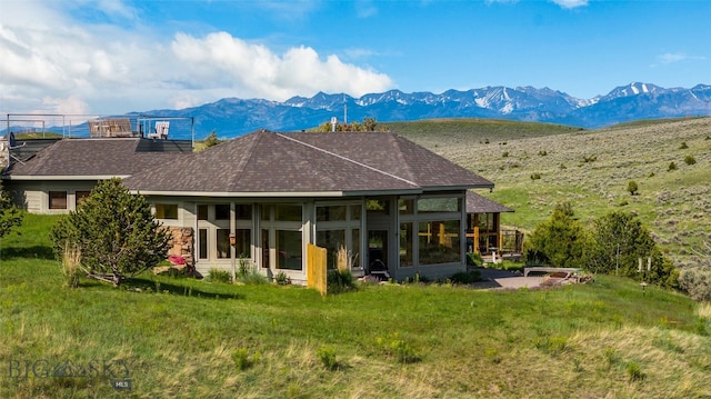 rear view of house featuring a sunroom, a mountain view, and a lawn