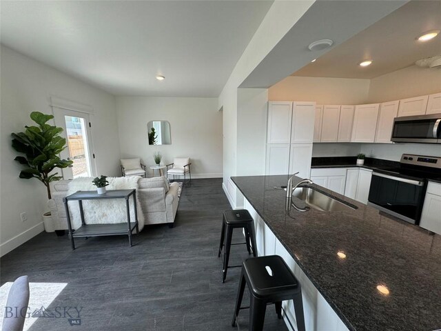 kitchen with white cabinetry, sink, dark stone countertops, a kitchen bar, and appliances with stainless steel finishes