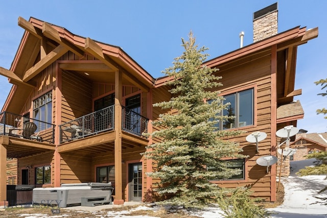 snow covered house featuring a balcony and a hot tub