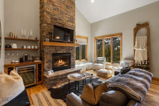 living room with a stone fireplace, wine cooler, light hardwood / wood-style floors, and high vaulted ceiling