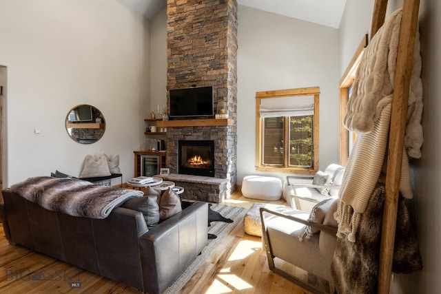 living room with light hardwood / wood-style floors, a stone fireplace, and high vaulted ceiling