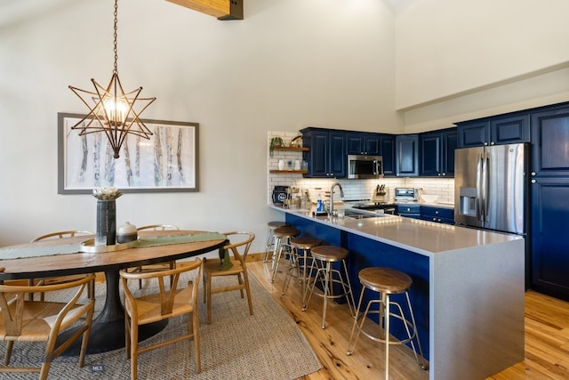 kitchen with light wood-type flooring, a notable chandelier, kitchen peninsula, stainless steel appliances, and blue cabinets