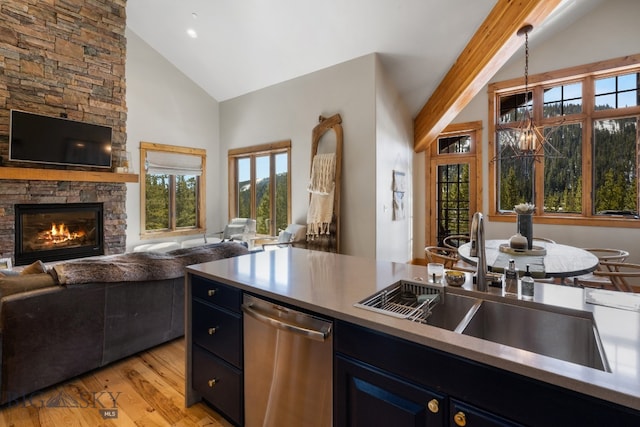 kitchen with sink, stainless steel dishwasher, a stone fireplace, blue cabinetry, and light hardwood / wood-style floors