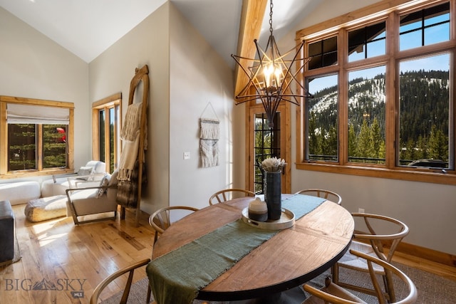 dining room with a notable chandelier, wood-type flooring, and high vaulted ceiling