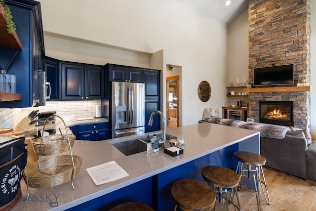 kitchen featuring a kitchen breakfast bar, blue cabinets, a stone fireplace, stainless steel appliances, and light wood-type flooring