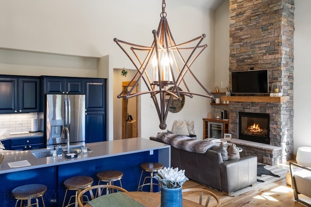 kitchen with a fireplace, blue cabinetry, light hardwood / wood-style flooring, stainless steel refrigerator with ice dispenser, and a chandelier