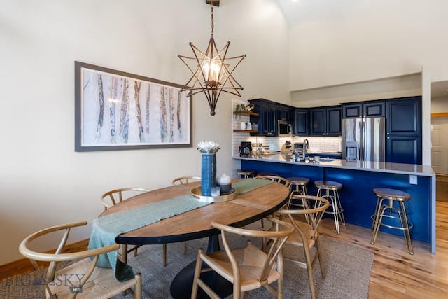 dining room with a high ceiling, light hardwood / wood-style floors, sink, and a notable chandelier