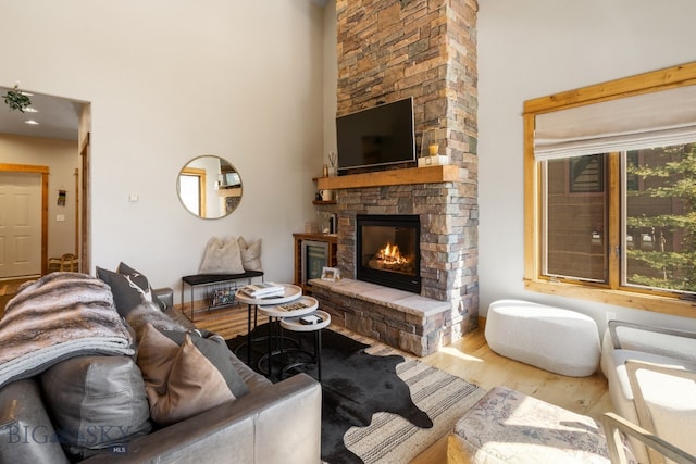 living room featuring wood-type flooring, a high ceiling, and a stone fireplace