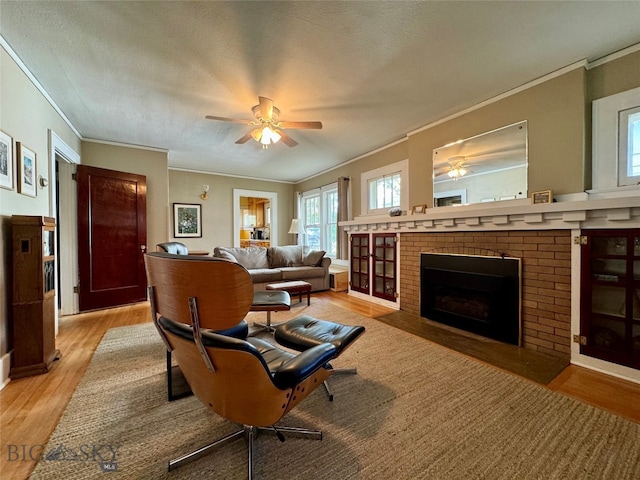 living room with a brick fireplace, crown molding, light hardwood / wood-style floors, and ceiling fan