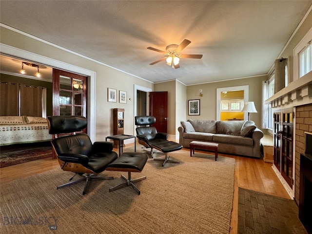 living room featuring a brick fireplace, a textured ceiling, wood-type flooring, crown molding, and ceiling fan