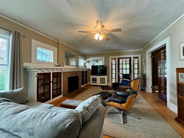 living room featuring ceiling fan, a brick fireplace, light hardwood / wood-style floors, and a wealth of natural light