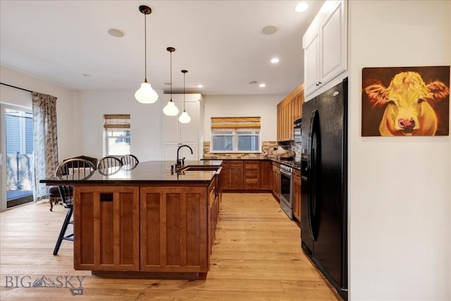 kitchen featuring light wood-type flooring, black fridge, a kitchen breakfast bar, a center island with sink, and decorative light fixtures