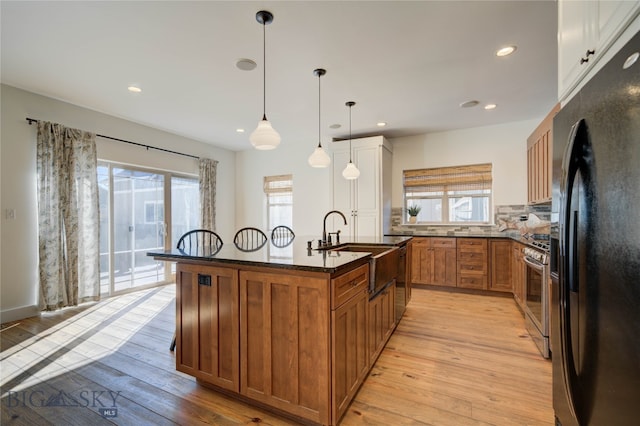 kitchen featuring a wealth of natural light, light hardwood / wood-style floors, a center island with sink, and black fridge