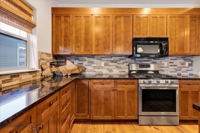 kitchen with backsplash, dark stone counters, light wood-type flooring, and gas stove