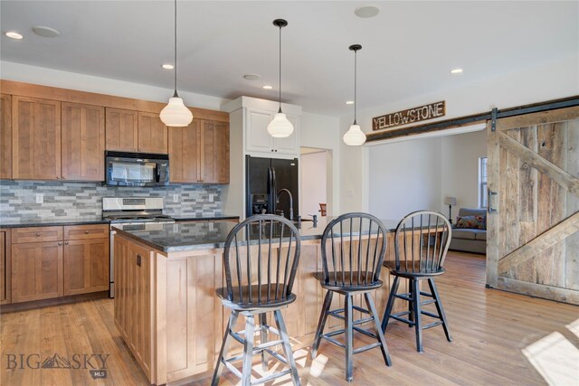 kitchen featuring a barn door, black appliances, light hardwood / wood-style floors, and an island with sink