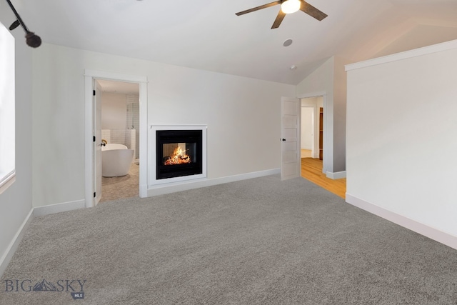 unfurnished living room featuring ceiling fan, a multi sided fireplace, light carpet, and vaulted ceiling