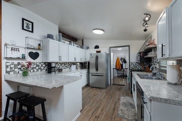 kitchen featuring white cabinetry, appliances with stainless steel finishes, sink, vaulted ceiling, and light hardwood / wood-style floors