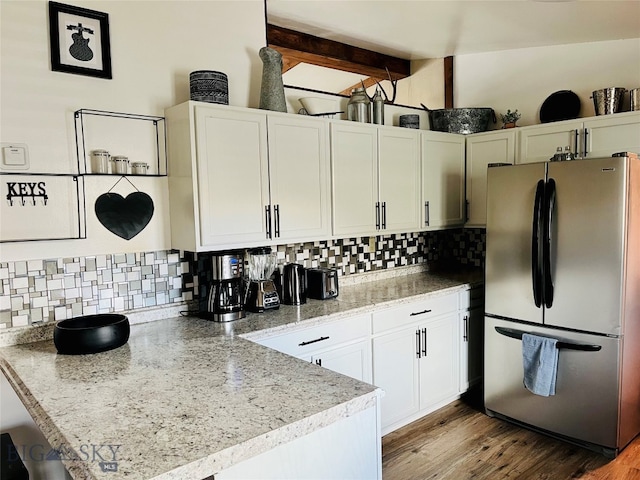 kitchen featuring light hardwood / wood-style floors, kitchen peninsula, backsplash, stainless steel refrigerator, and white cabinetry