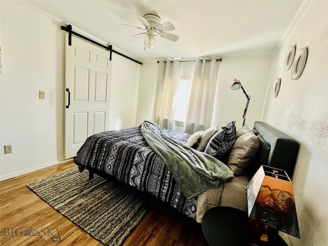 bedroom with ornamental molding, dark hardwood / wood-style flooring, a barn door, and ceiling fan