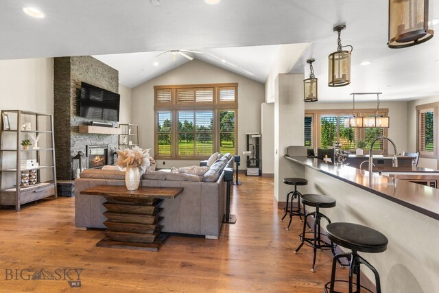 living room with hardwood / wood-style floors, ceiling fan, vaulted ceiling, and a fireplace