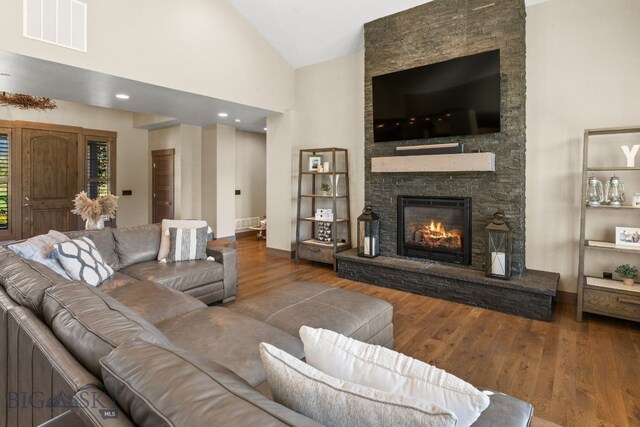 living room with high vaulted ceiling, hardwood / wood-style flooring, and a stone fireplace