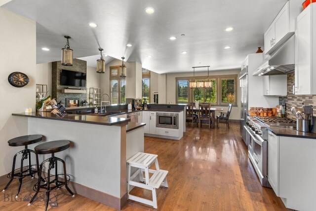 kitchen with kitchen peninsula, a breakfast bar, decorative light fixtures, appliances with stainless steel finishes, and a large fireplace