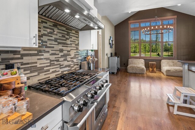 kitchen featuring decorative backsplash, vaulted ceiling, white cabinets, range with two ovens, and wall chimney range hood