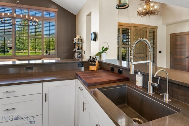 kitchen with hanging light fixtures, white cabinetry, lofted ceiling, sink, and a chandelier