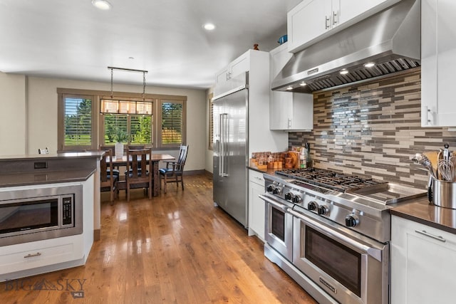 kitchen featuring white cabinetry, built in appliances, and decorative light fixtures