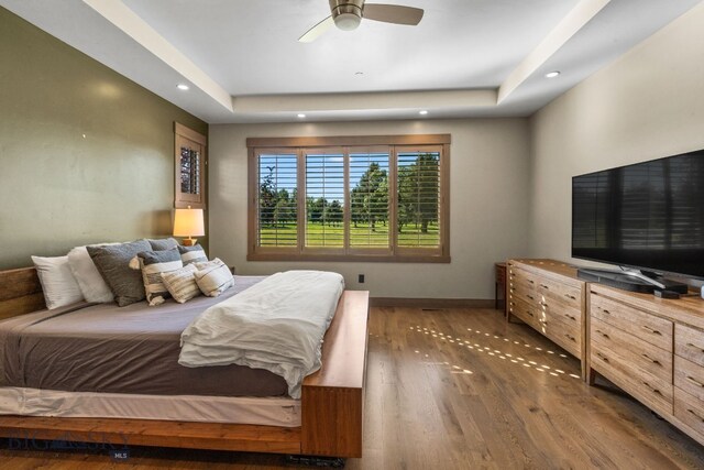 bedroom with a tray ceiling, ceiling fan, and dark wood-type flooring