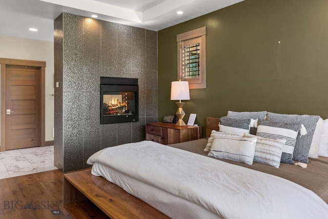 bedroom with a multi sided fireplace and light hardwood / wood-style floors