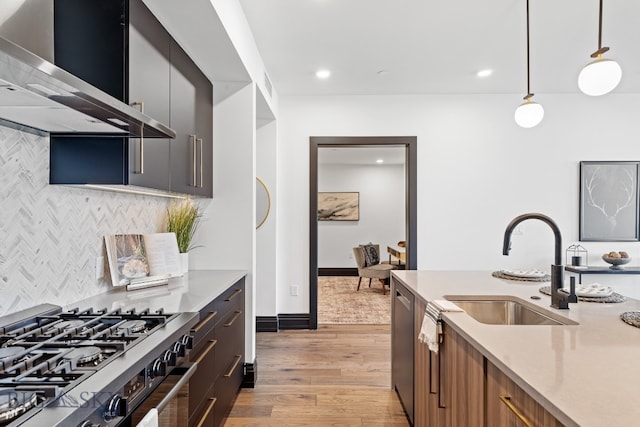 kitchen with wall chimney range hood, appliances with stainless steel finishes, light wood-type flooring, pendant lighting, and sink