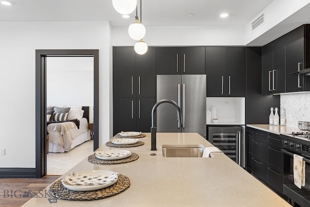 kitchen featuring hardwood / wood-style flooring, black range with gas stovetop, pendant lighting, beverage cooler, and stainless steel refrigerator