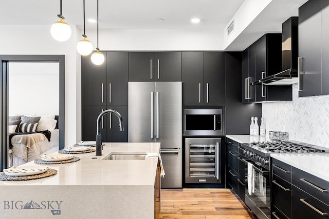 kitchen with extractor fan, light hardwood / wood-style flooring, pendant lighting, beverage cooler, and appliances with stainless steel finishes