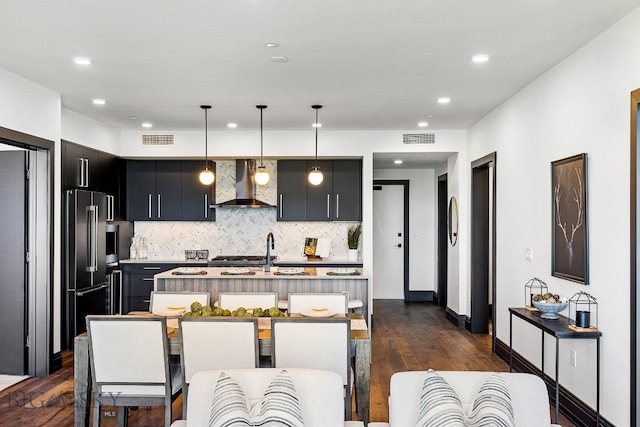 kitchen featuring wall chimney range hood, dark hardwood / wood-style flooring, a kitchen breakfast bar, decorative light fixtures, and high quality fridge