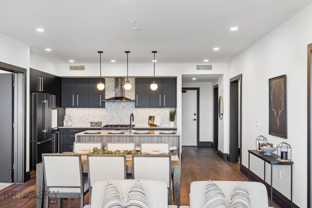 kitchen featuring dark wood-type flooring, a breakfast bar, wall chimney exhaust hood, pendant lighting, and high end fridge