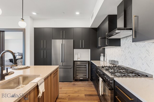 kitchen featuring appliances with stainless steel finishes, light hardwood / wood-style floors, wine cooler, wall chimney exhaust hood, and decorative light fixtures