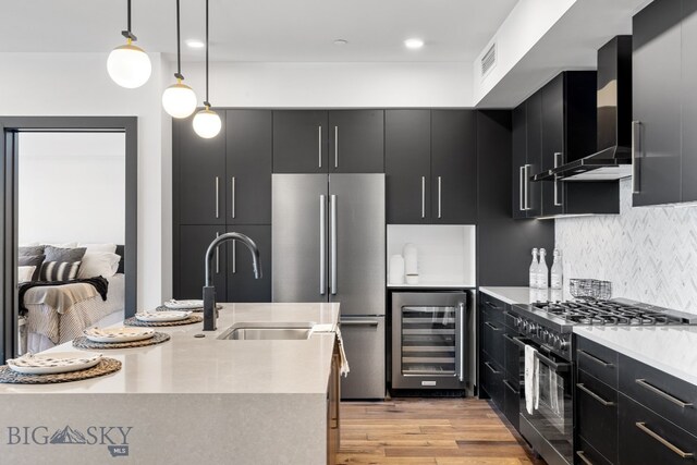 kitchen with wine cooler, light hardwood / wood-style floors, wall chimney range hood, appliances with stainless steel finishes, and decorative light fixtures